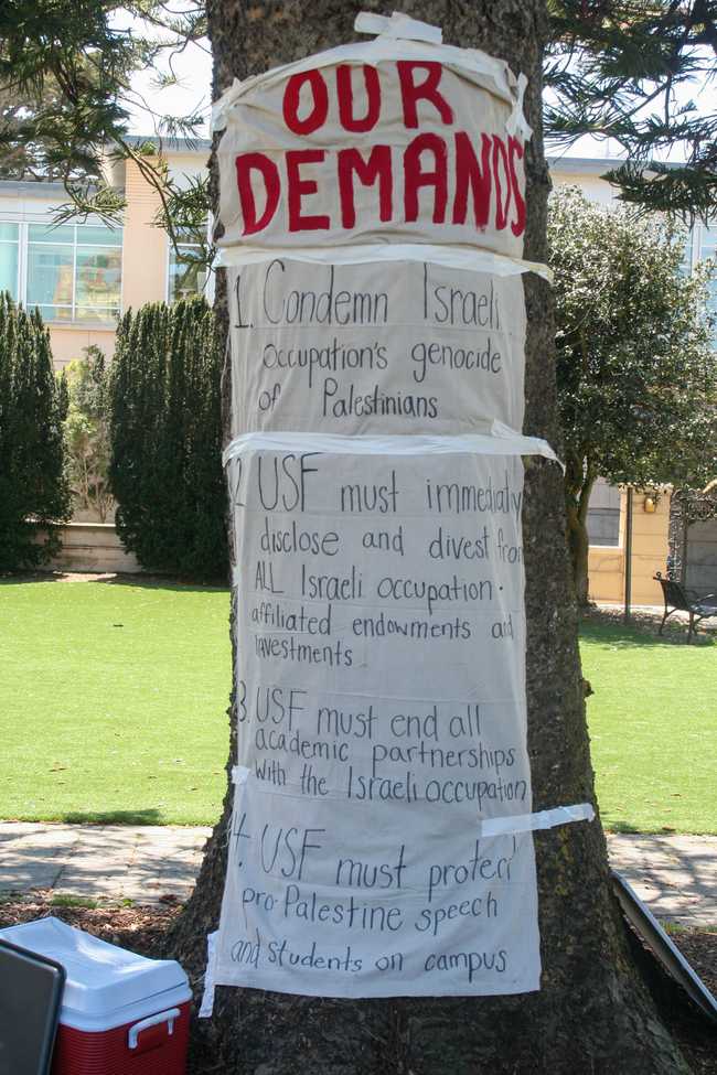 a sign reading: 1. Condemn Israeli occupation's genocide of Palestinians 2. USF must immediately disclose and divest from all Israeli occupation affiliated endowments and investments 3. USF must end all academic partnerships with the Israeli occupation 4. USF must protect pro-Palestine speach and students on campus